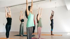 a group of women doing yoga poses in a room with their arms up and hands raised