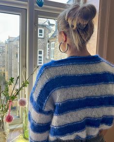 a woman standing in front of a window next to a vase filled with flowers and looking out the window