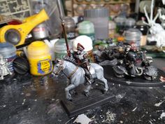 two toy soldiers riding on horses in front of other toys and items that are sitting on the table