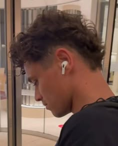 a young man wearing ear buds looking at his cell phone in front of a glass door