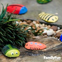 small plastic fish sitting on top of rocks next to plants and stones with grass growing out of them