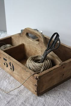 a pair of scissors and rope in a wooden box on a bed with white sheets