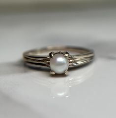 a close up of a ring with a pearl in it on a white table top