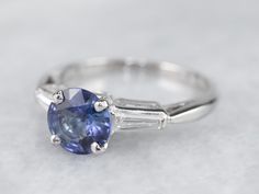 This vintage sapphire and diamond engagement ring is the epitome of a classic! This intense blue sapphire is a perfect, rich color, the benchmark for a fine sapphire. The crisp blue hue is filled with glitter and it has phenomenal light refraction, depth of color, and sparkle on the finger! We've set this in a tasteful platinum mounting featuring baguette diamonds on either side, equal in quality and sparkle to this lovely center sapphire. The ring was originally designed as an engagement piece, Classic Gia Certified Sapphire Ring, Classic Blue Sapphire Ring In Platinum, Timeless Blue Sapphire Ring Gia Certified, Timeless Baguette-cut Sapphire Ring, Timeless Round Cut Sapphire Ring, Timeless Gia Certified Blue Sapphire Ring, Classic Sapphire Tanzanite Solitaire Ring, Classic Tanzanite Solitaire Sapphire Ring, Timeless Sapphire Ring In Platinum