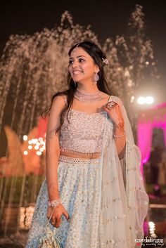 a woman in a white and blue lehenga standing next to a fountain at night