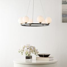 a white table with flowers and books on it next to a wall mounted light fixture