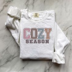 Fall Sweatshirt, Cozy Season Fall Sweatshirt, Cozy Season Merry Christmas, Christmas Sweatshirt, Winter Sweatshirt, Stay Home, Cozy Vibes Embrace the cozy vibes of fall and winter with our "Cozy Season" sweatshirt! Perfect for snuggling up at home, sipping hot cocoa, or celebrating the holidays in style. This soft and warm sweatshirt is your ultimate companion for chilly days and nights.  Available in festive "Merry Christmas" designs and classic fall styles. Luxurious comfort and style are what this unisex, garment-dyed sweatshirt is all about. It's made with 80% ring-spun cotton and 20% polyester and the fabric is 3-end garment-dyed, ring-spun, color-blast fleece with a 100% cotton face. Each sweatshirt comes with a relaxed fit, a rolled-forward shoulder, and a back neck patch.  .: 80% r Cozy Cotton T-shirt For Loungewear, Long Sleeve T-shirt For Winter Loungewear, Cozy Cotton Sweater, Cozy Crew Neck T-shirt For Loungewear, Cozy Fit Cotton Sweatshirt, Cozy White Graphic Print T-shirt, Comfy Winter Loungewear Tops, Cozy Sweatshirt For Fall Holiday, Cozy Sweatshirt For Holiday And Fall