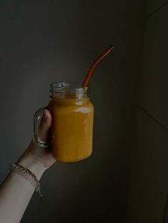 a hand holding a glass jar filled with orange liquid and a wooden straw sticking out of it