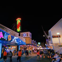 people are walking around in front of the neon sign for an amusement park at night