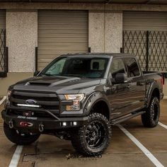 a black truck parked in a parking lot next to a building with garage doors open