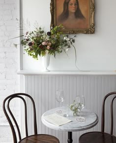 two chairs and a table in front of a painting on the wall with flowers next to it