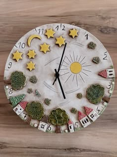 a clock made out of clay with stars, moon and houses on the face is sitting on a wooden surface