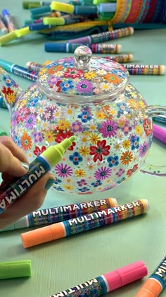 colorful crayons are lined up in front of a teapot with flowers on it