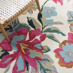 a white rug with pink, blue and green flowers on it next to a chair