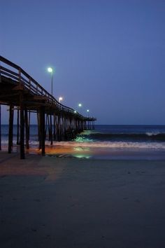 the pier is lit up at night with lights on and waves coming in from the ocean