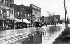 an old black and white photo of people riding horses in the rain on a city street