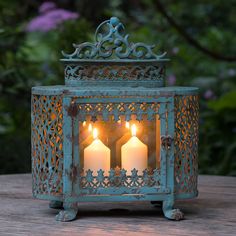 two lit candles are in an ornate metal box with filigrees on the sides