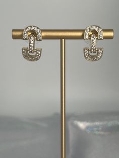 The Gold CZ Huggie Earrings are the epitome of elegance and sparkle, featuring a sleek gold finish on a snug, huggie design that's lavishly adorned with cubic zirconia stones for an irresistible glitter. These earrings are a perfect blend of sophistication and glamour, designed to hug the earlobe gently, making them an ideal accessory for both day-to-day elegance and special occasions. Length: 21.5 mm Width: 11.1 mm Closure: Bullet with Disc Backs Material: Brass with 18K Gold Plating with Rhodi Luxury Hinged Huggie Earrings, Gold Cubic Zirconia Crystal Earrings With Bling, Modern Gold Diamond Earrings For Party, Gold Cubic Zirconia Clip-on Earrings For Party, Modern Gold Earrings With Sparkling Stones, Dazzling Gold Metal Earrings, Chic Sparkling Gold Earrings, Gold Metal Hoop Earrings With Sparkling Stones, Classic Gold Huggie Earrings With Sparkling Stones