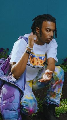 a man with dreadlocks sitting on the ground in front of a blue wall