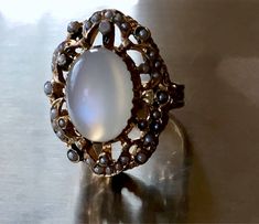 this ring is just incredible!! please see photos! crafted in solid heavy 14k yellow gold and very ornate plus dark enamel and real pearl seeds around!! the rest of enamel is present around the pearls and on the prongs! the pearls are all different in shape and size - because they are natural. all pearl seeds are present, no visible wear to the moonstone! the moonstone is clean and very chatoyant! )with strong chatoyancy effect! - which moves from one side to another as you move your hand!) ! the Antique Pearl Ring With Gemstone, Heirloom Oval Moonstone Ring, Collectible Oval Cabochon Moonstone Ring, Antique Moonstone Oval Cabochon Ring, Antique Oval Cabochon Moonstone Ring, Victorian Oval Cabochon Pearl Ring, Antique Oval Hallmarked Moonstone Ring, Antique Oval Moonstone Ring Collectible, Antique Oval Moonstone Ring Hallmarked