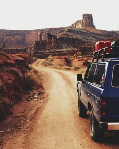 a blue truck parked on the side of a dirt road in front of a mountain