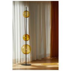 three yellow glass balls on a black metal stand in front of curtains and drapes