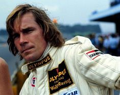 a man with long hair wearing a racing suit and holding his hand out to the side