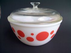 a red and white bowl sitting on top of a black table next to a glass container