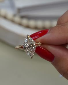 a woman's hand holding a diamond ring with red nails on her fingers,