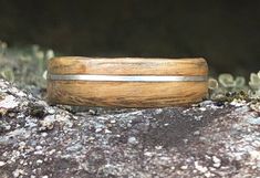 a wooden ring sitting on top of a rock covered in moss and dirt with a metal stripe