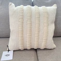 a white pillow sitting on top of a gray couch next to a tag that says gg