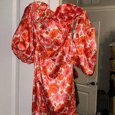 an orange and red floral print dress hanging on a clothes rack in front of a door