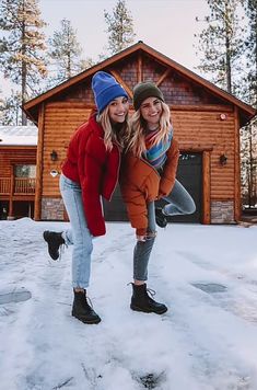 two young women are posing in front of a log cabin with snow on the ground