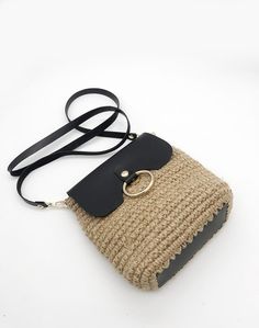 a straw bag with a black handle and gold ring on the front, sitting on a white surface