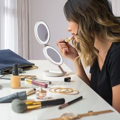 a woman sitting at a table looking into a mirror with makeup and brushes on it