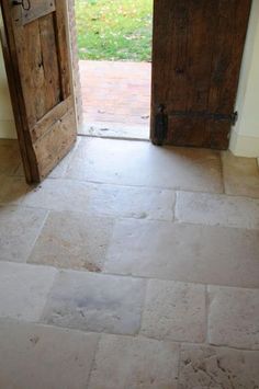 an open wooden door with stone flooring next to a brick wall and green grass