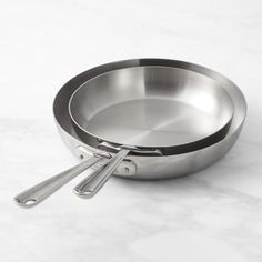 two stainless steel pans with tongs on a marble countertop, ready to be used as cooking utensils