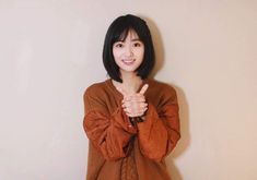 a woman standing in front of a white wall giving the peace sign with her hand