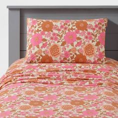 an orange and pink floral bed spread with matching pillow cases on a gray headboard