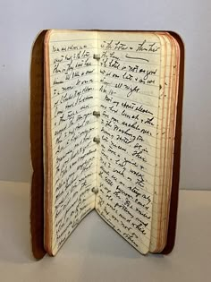 an open book with writing on it sitting on top of a white table next to a wall