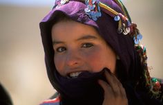 a woman wearing a purple hat and scarf talking on her cell phone while looking at the camera