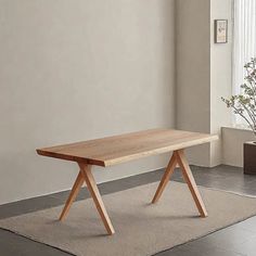 a wooden table sitting on top of a rug in front of a window next to a potted plant