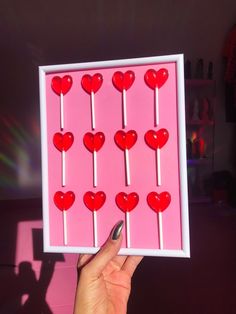 a person holding up a box with lollipops in the shape of hearts