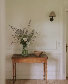 a wooden table topped with a vase filled with flowers next to a wall mounted light