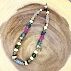 a necklace with multicolored beads is displayed on a wooden surface in front of a piece of wood