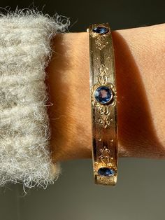 "Delicate and radiant, this one of a kind sapphire bangle would have made an unforgettable gift. Engraved on the rear of the bangle are the words \"Ultima from pop pop 1914\". The engraving on the rear matches the grace of the engraved design on the front. Both of these details are complimented by the use of faceted cornflower blue sapphires which have been bezel set. Estimated total sapphire weight 1.2 carats 14k gold 7mm thickness 60mm diameter 12.8 grams Carries engraving \"Ultima from pop po Sapphire Bangle Bracelet For Formal Occasions, Luxury Oval Bangle For Anniversary, Oval Gemstone Bangle For Formal Events, Formal Jeweled Cuff Bangle Bracelet, Formal Jewel Bangle Cuff Bracelet, Luxury Jeweled Bangle, Classic Gemstone Bangle For Anniversary, Classic Formal Bangle With Gemstone, Heirloom Bangle With 17 Jewels For Anniversary