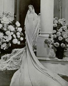 an old black and white photo of a woman in a wedding dress standing next to flowers