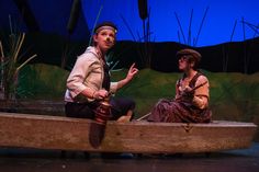 a man and woman sitting in a boat on stage