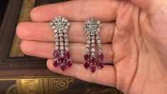 These lovely dangle style pierced earrings are each accented with three (3), prong set, baguette cut diamonds, thirty-three (33), prong set, round brilliant cut diamonds and six (6), prong set, oval mixed cut natural rubies. The earrings measure 42mm X 15mm and are finished with friction style backs. Elegant White Gold Diamond Earrings With Baguette Diamonds, Luxury Baguette Cut Diamond Earrings For Formal Occasions, Elegant Baguette Diamond Earrings For Anniversary, Luxury Formal Baguette Cut Diamond Earrings, Classic Baguette Diamond Earrings For Formal Occasions, Luxury Diamond Earrings With Baguette Cut, Classic Brilliant Cut Chandelier Earrings For Anniversary, Luxury Baguette Cut Diamond Earrings With Accents, Luxury Bridal Earrings With Baguette Diamonds For Anniversary