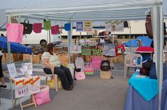 two women sitting under a tent at an outdoor market